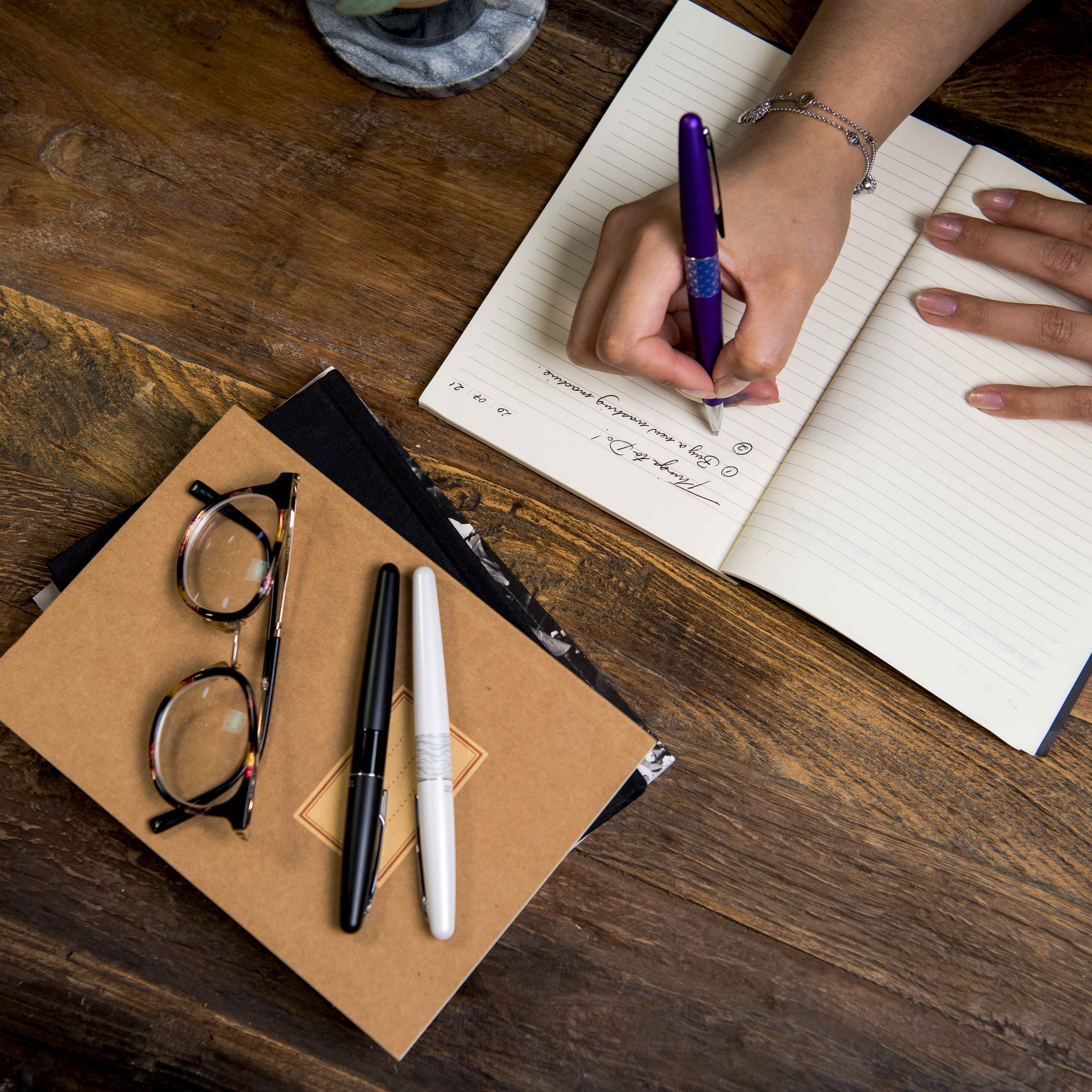 Top-down view of a hand writing with a luxury MR2 Animal Print Premium Ballpoint pen in Deep Purple Leopard body colour, showing an elegant design and smooth ink flow. White Tiger and Black Crocodile prints are visible on top of the notepad.