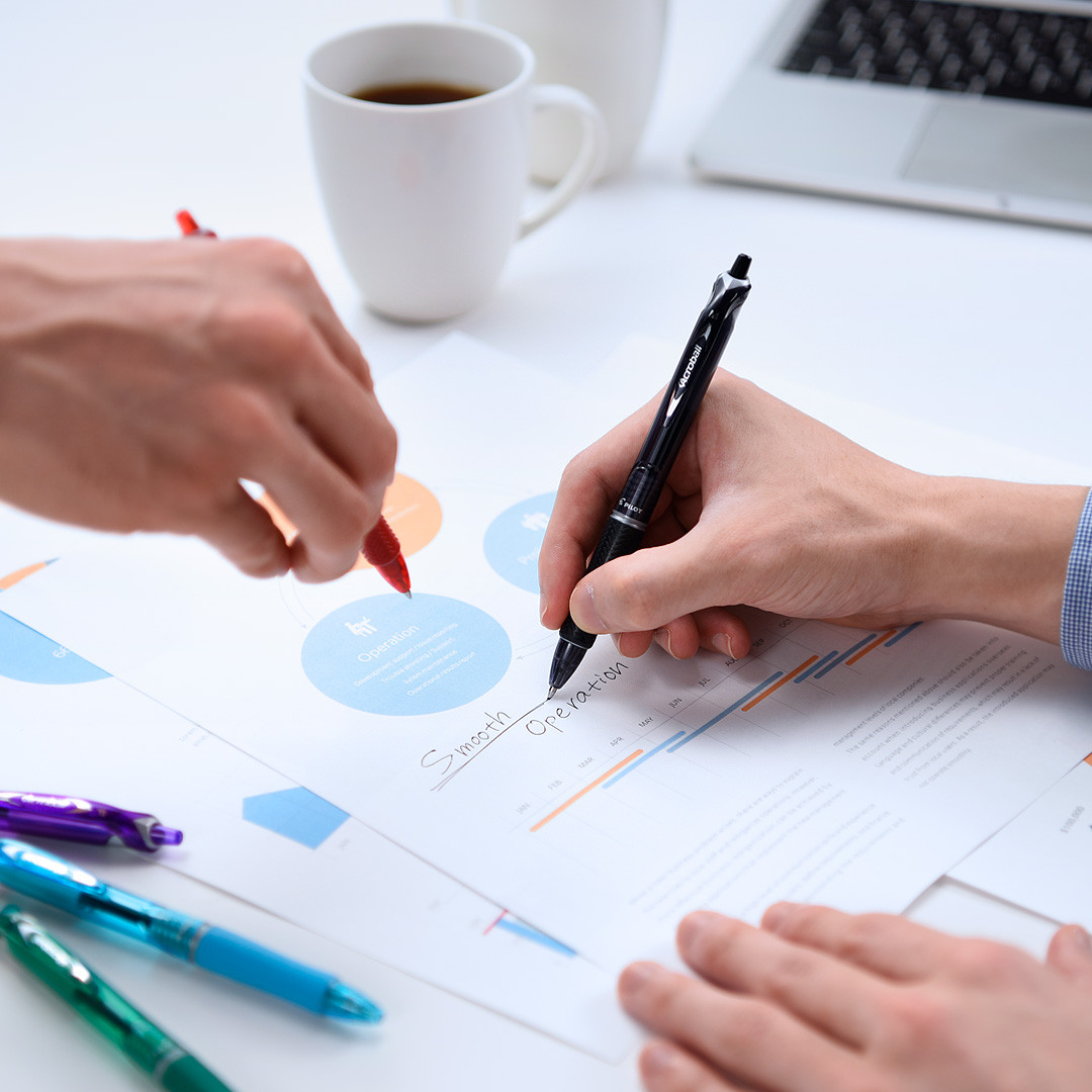 Two professionals using PILOT Acroball pens to mark up an important document, showcasing their smooth design and smear-resistant archival ink.