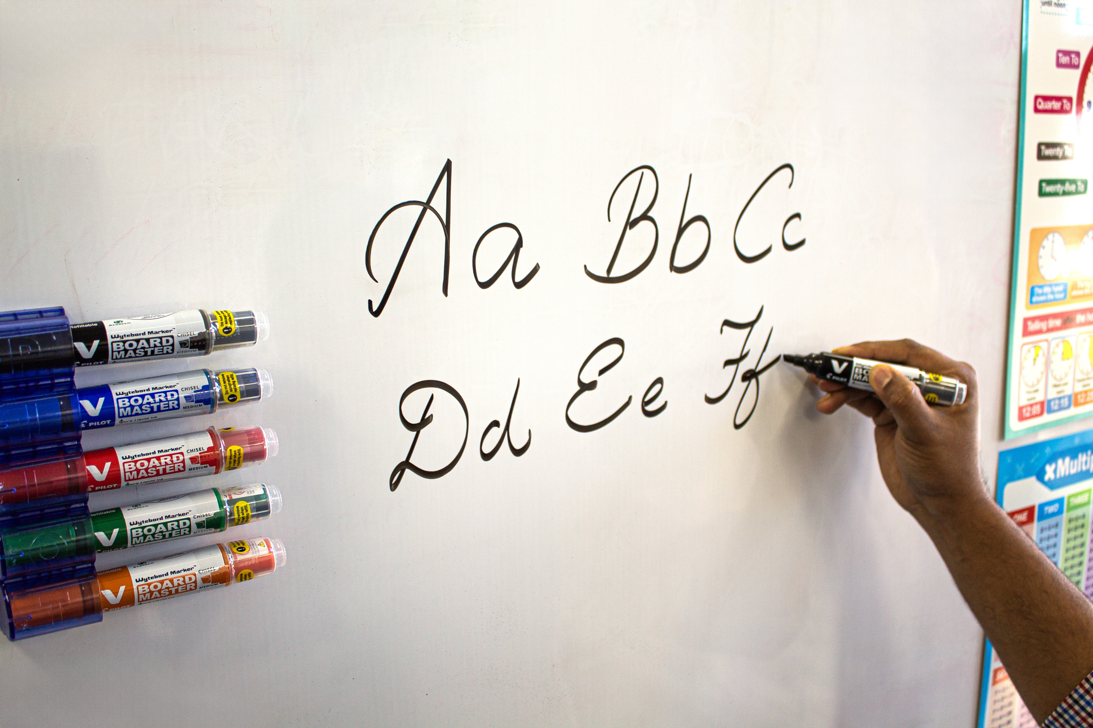 Teacher using a black Pilot V Board Master markers to write letters on a whiteboard, ideal for classrooms and promoting sustainable learning tools.