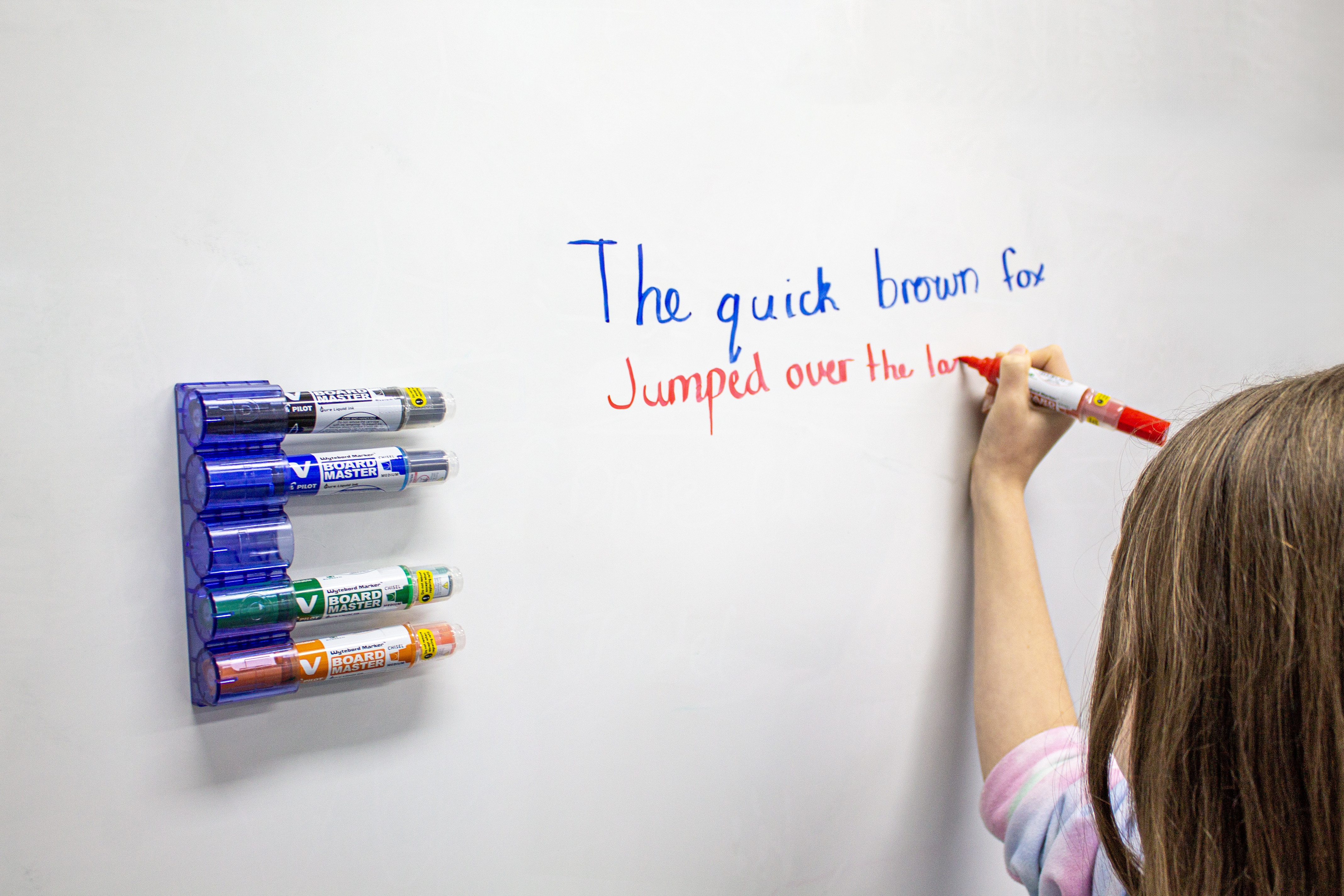 Student writing on a whiteboard with bold, vibrant colours using the blue and red Pilot V Board Master marker, showcasing its eco-friendly refillable design.