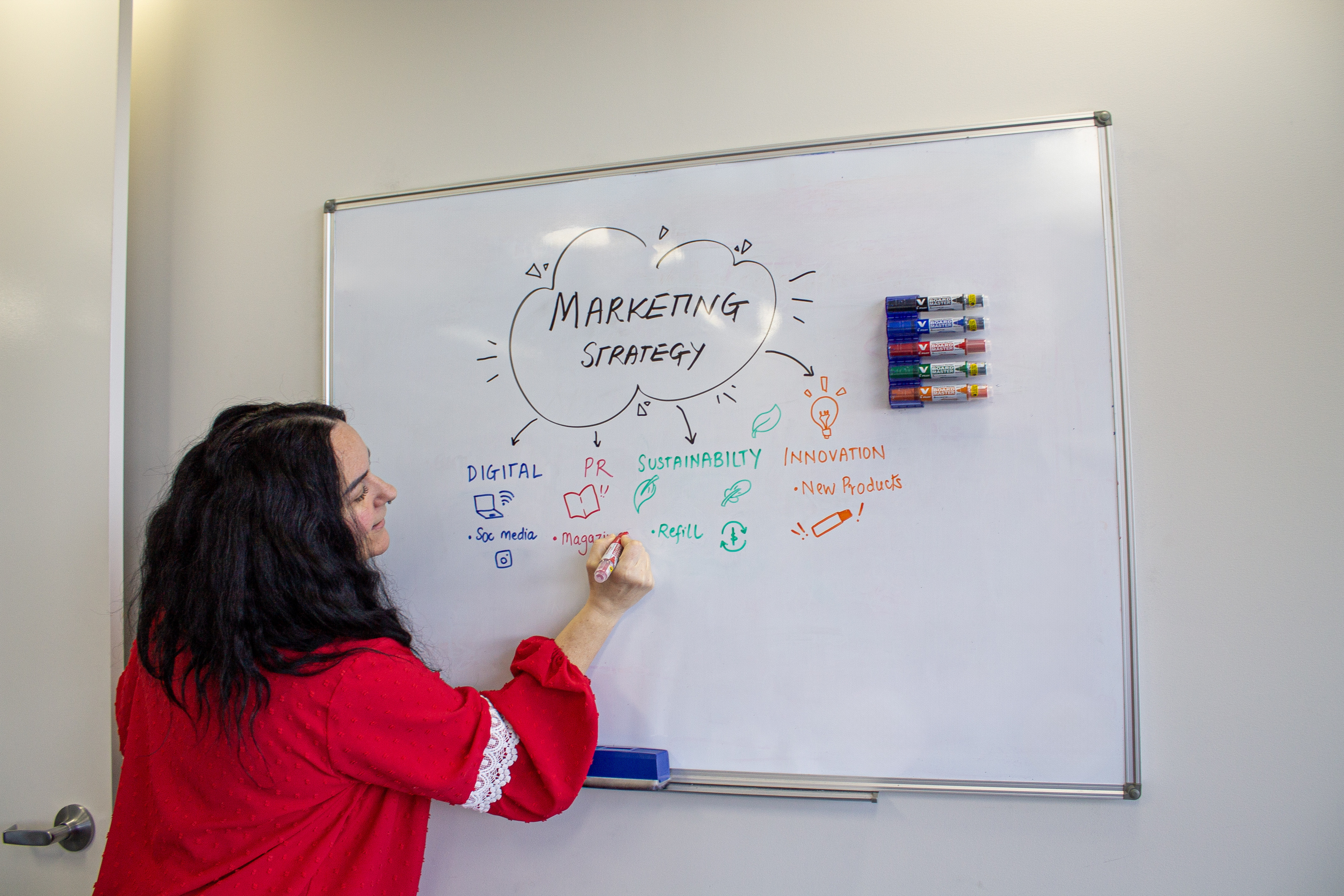 Woman brainstorming a marketing strategy on a whiteboard using Pilot V Board Master refillable markers, highlighting bold colours and eco-friendly design.