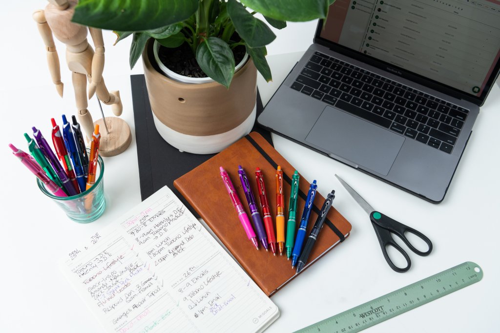 A variety of Pilot Acroball pens on a student's desk with a laptop and stationery.