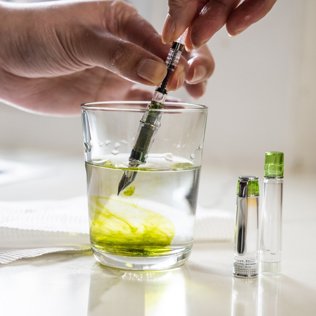 Pilot Prera fountain pen being cleaned in a glass of water with a paper towel behind it.